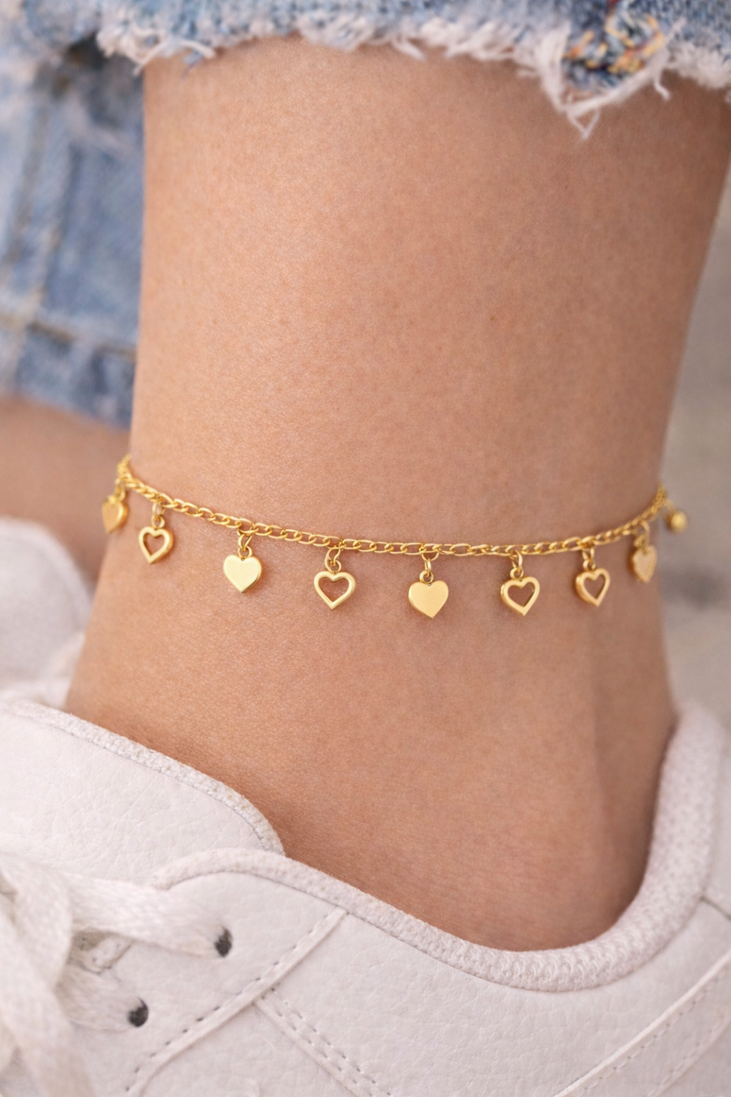 Heart dangle anklet with alternating filled and open heart charms worn on ankle